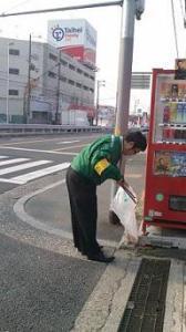ゴミ袋を持ったクロネコヤマトの男性社員が自販機傍のごみを集めている様子の写真