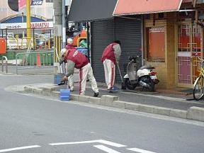 大阪トヨタLOGI&B-TEC株式会社の社員の方たちがシャッターの閉まった家屋の前でごみを集めている様子の写真