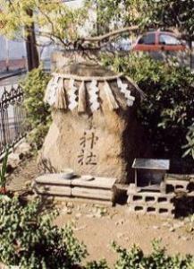 大きな岩にしめ縄が飾られ、岩の前には飲み物などが供えられ、野神さんが祀られている写真