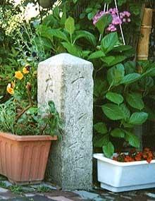 道標の後ろにアジサイの花が咲いており、周りには黄色い花や赤い花の咲いたプランタが飾られている写真