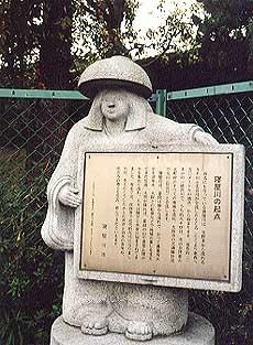 鉢かつぎ姫の形をした石像が「寝屋川の起点」が書かれた説明看板を持っている写真