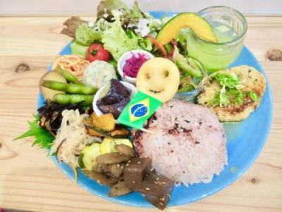 水色の大きなお皿にご飯にジュース、野菜にハンバーグなど18種類のおかずがのったワンプレートの写真