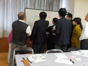 8名の参加者がホワイトボードの前に集まって話し合っている写真