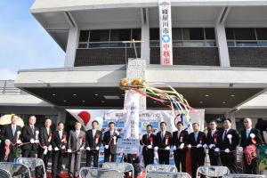 中核市移行式でくす玉が割られ、関係者の方々がテープを持ち一列に並んでいる写真
