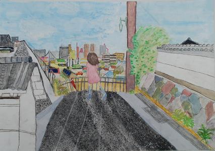 道路の端に女の子がたち、奥にはビルが立ち並ぶ青空の作品の写真