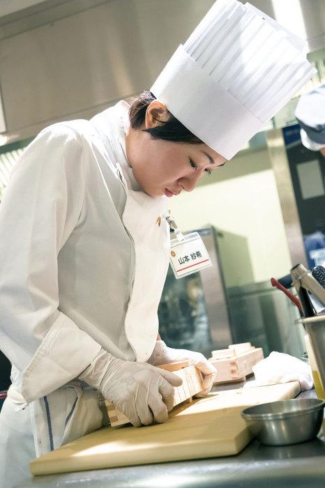 コックコートにコック帽を被り調理場に立っている山本紗希さんの写真