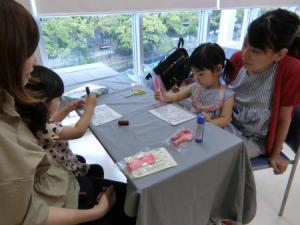 お母さんの膝の上に座り、机の上にある遊び道具で遊んでいる子供たちの写真