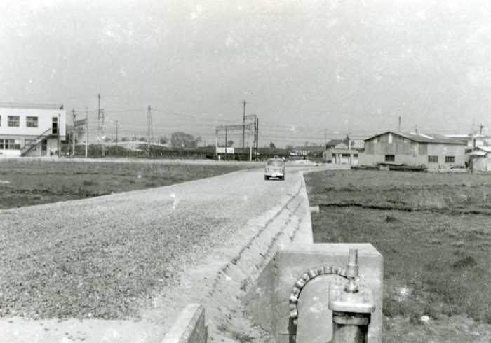 中央に真っ直ぐ伸びる道路を一台の車が走っています。道路の両脇は広々とした空き地が広がっている写真