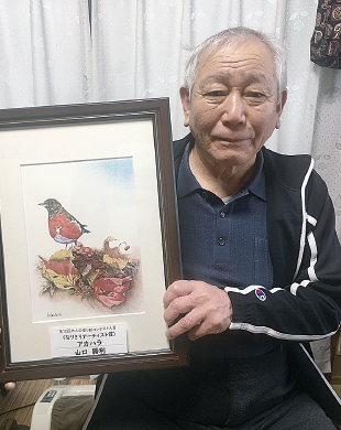 色鉛筆で鳥を描いた作品を持っている山口勝利さんの写真