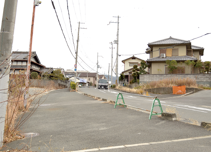 緩やかカーブの坂道で歩道が広くとられており、道路添いには住宅が並んでいる現在の写真