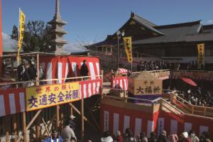 紅白の横断幕で飾られた成田山不動尊のやぐらの下に大勢の人々が集まっている写真