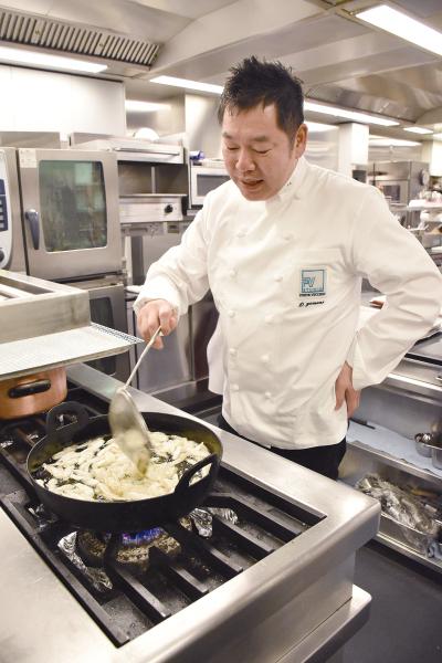 調理場で白衣を着て揚げ物をしている山根大助さんの写真