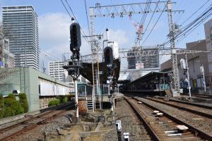 左側にレールが追加され、右側には平行に2本のレールが敷かれ、停車場があり、後方には大きなビルが建ち並んでいる写真