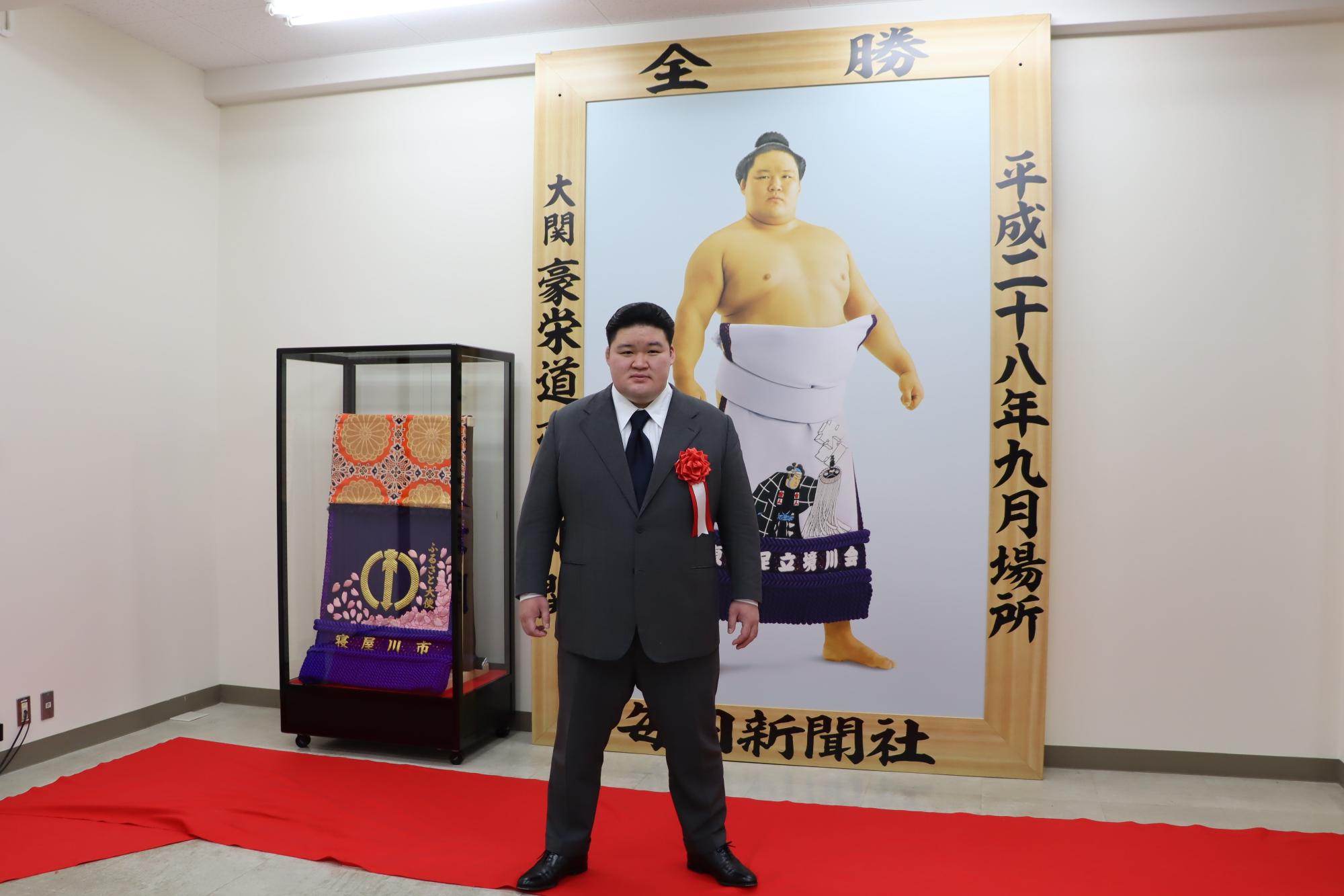 優勝額、化粧まわしと一緒に映っている武隈親方の画像