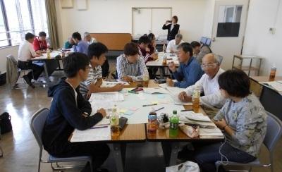 テーブルには資料や飲み物が置いてあり、話し合いをするワークショップ会議の全体写真