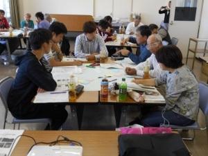 テーブルには資料や飲み物が置いてあり、話し合いをする6人の写真