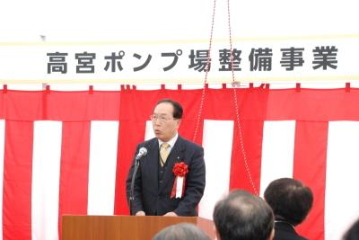 紅白幕の上に高宮ポンプ場整備事業と書かれた貼り紙の前の壇上で、北川市議会議長が挨拶を行っている写真