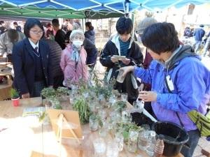 植物が入っているカップが並び、体験ブースに5人の人が集まる写真