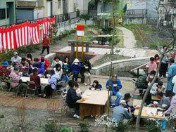 公園づくりが完成し、園内に木製のテーブルを設置し周囲のパイプ椅子に腰かけた市民が、イベントで振舞われた食べ物を食している様子を上から撮影した写真