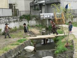 4名の子ども達が、小川に設置された桟橋を渡っている写真