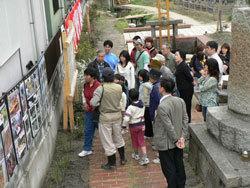 紅白幕が掛けられている手前に写真が飾っており、イベントに参加した市民に説明を行っている写真