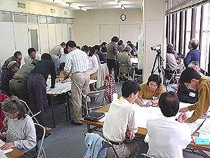 右側に大きなガラス窓のある会議室内で、参加者がグループごとに分かれてワークショップを行っている様子の写真