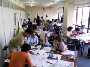 会議室内に長机を繋げた島にグループになって参加者が座り、ワークショップを行っている様子の写真