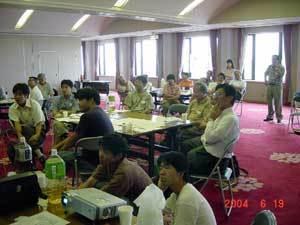 グループごとに分かれて座っている参加者と、プロジェクターで映像を写している大学生が座って話しを聞いている写真