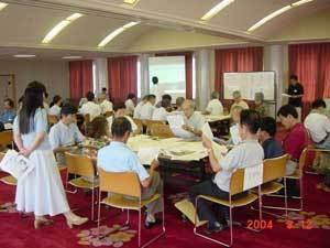 グループごとに分かれて座っている参加者たちが資料を手に持ち話しを聞いている写真