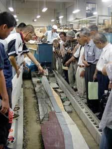 コンクリートブロックを横一列に並べた、大きな駅前親水河川空間の模型を挟み参加者たちが立ち説明を受けている写真