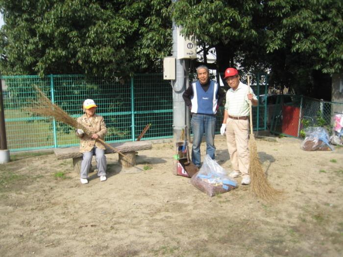 公園のベンチに座っている帽子を被り箒を持った女性、青いベストを着ている西岡さん、赤い帽子を被り箒を持った大村さんが写っている写真