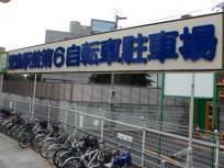 「萱島駅前第6自転車駐車場」と青文字で記された看板の下に金網で柵がしてありたくさんの自転車が駐輪されている駅前第6自転車駐車場の写真