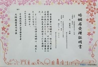 赤い糸とまちのイラストが繋がって描かれており、全体にさくらの花びらが描かれている婚姻届受理証の写真