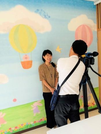 1人の女性がカメラの前に立ち取材を受けている写真