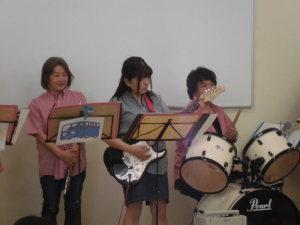 フルート担当のメンバー、ギターを弾いているメンバー、ドラムをたたいているメンバーの写真