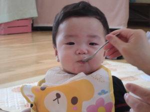 くまの絵がかいてある前掛けをして離乳食を食べてる子供の写真