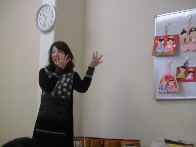 手作りのお内裏様とお雛様が飾られているホワイトボードの横で手遊びをしながら歌っている末吉先生の写真