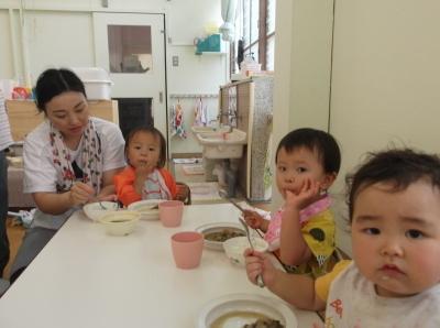 スプーンを使って給食を食べている子供たちと子供に食べさせている母親の写真