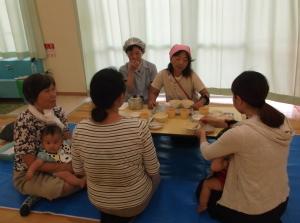 テーブルに並んだ離乳食の見本を見ながら説明する先生と話を聞いている母親の写真