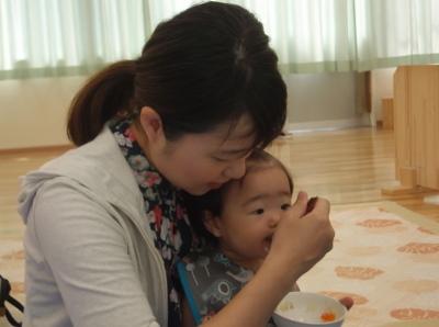 子供を膝の上に座らせて離乳食を食べさせている母親の写真