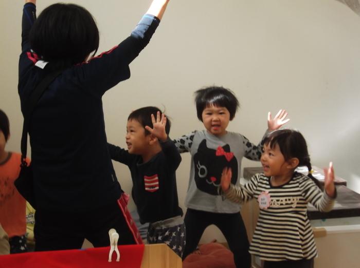 大きく両手を広げて笑顔で踊っている3人の子供たちと先生の写真