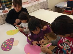 画用紙で作ったキノコにピンクや黄色や緑色のシールを貼っている二組の親子の写真