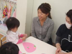 ピンク色の画用紙にシールを貼っている子供と横で見守っている母親の写真