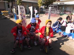 さつまいものイラストと「やきいも」の文字がかいてある幟がついた三輪車に乗っている、赤い法被を着た4人の子供たちの写真