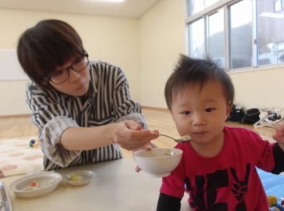 子どもの口元に離乳食がのったスプーンを近づけて食べさせようとしている母親の写真