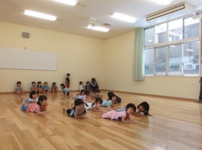 教室の床に腹ばいになって寝そべっている子供たちと教室の隅に座っている子供たちの写真