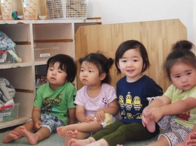 教室の床に横に並んで足を伸ばして座っている4人の子供たちの写真