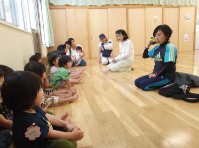 子供たちの前で話をしている先生、横一列に並んで座って話を聞いている子供たちと体験参加者の二組の親子の写真