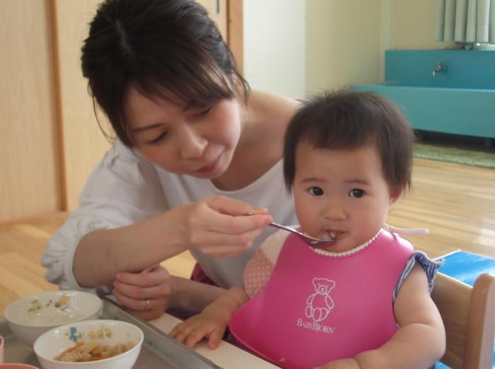 子供の口元にスプーンを持っていき離乳食を食べさせている母親の写真