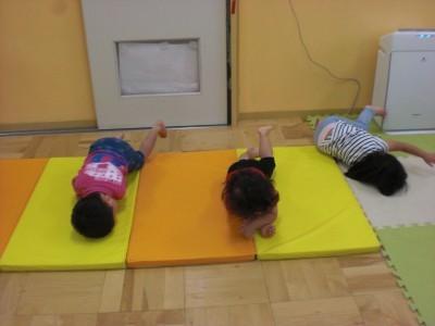 マットの上でドングリになりきってゴロゴロと転がっている3人の子ども達の写真